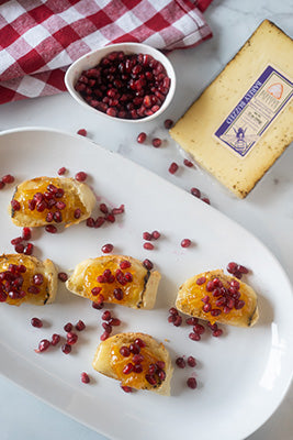Five crostinis on a white platter sprinkled with pomegranate seeds  