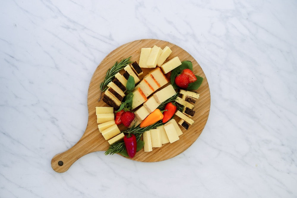 A circular board with cut cheeses garnished with greenery.