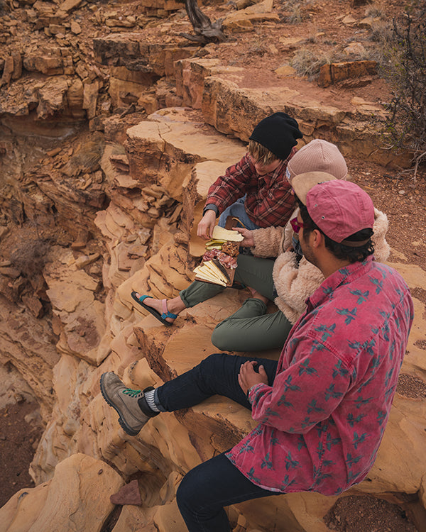 Three friends eating cheese on a red rock cliff