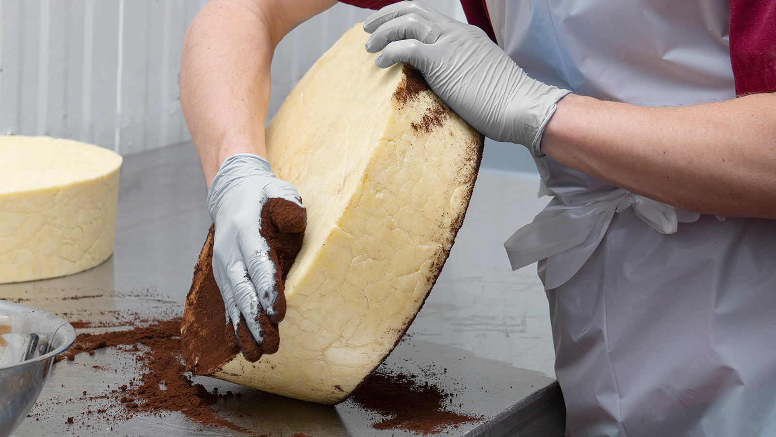 A gloved hand rubbing coffee on a 20 pound wheel of cheddar
